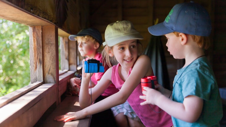 children sit in a bird hide holding binoculars.